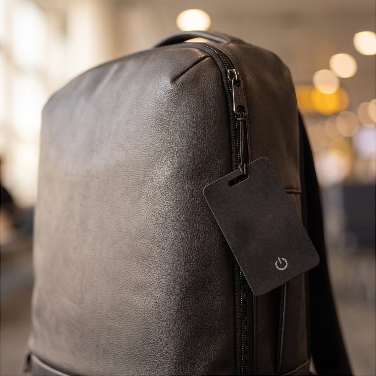 LYNK Card Tracker hanging from the zip pull of a leather backpack on a city street